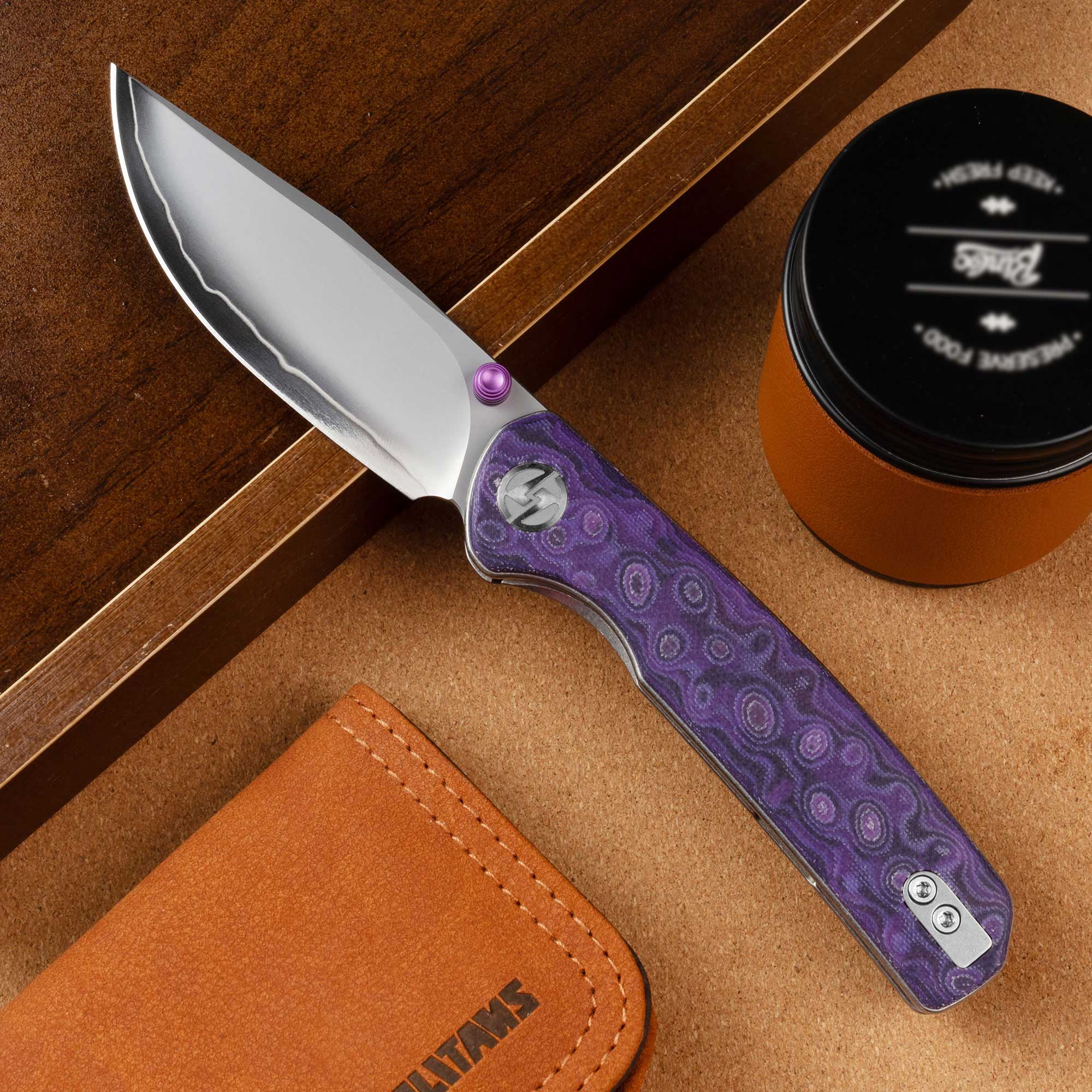 Open OLITANS Gecko SE G080 Purple Micarta knife displayed with leather accessories