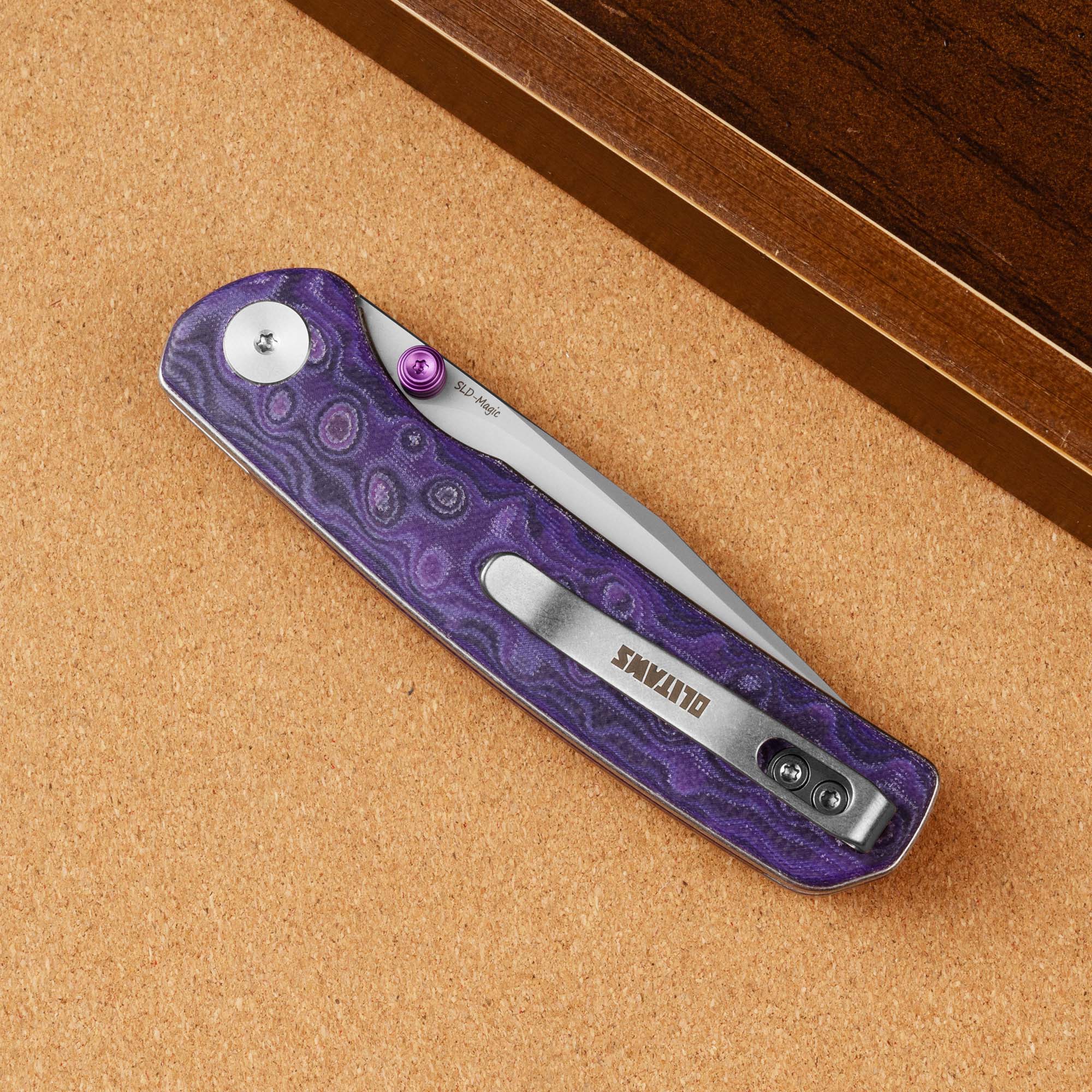 Closed OLITANS Gecko SE G080 Purple Micarta knife on a brown display surface